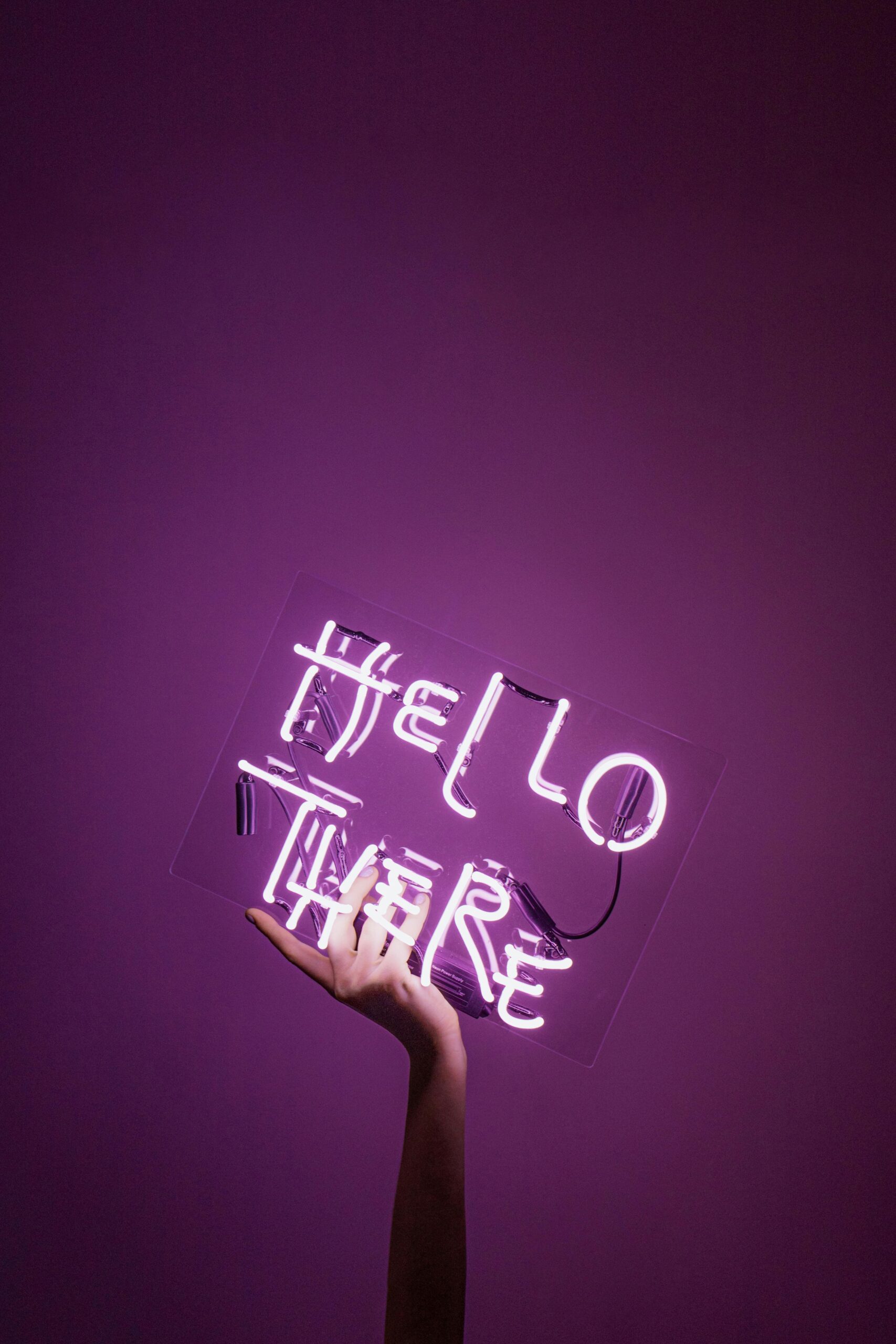 A hand holding a neon sign with the text 'Hello There' against a purple background, creating a vivid contrast.